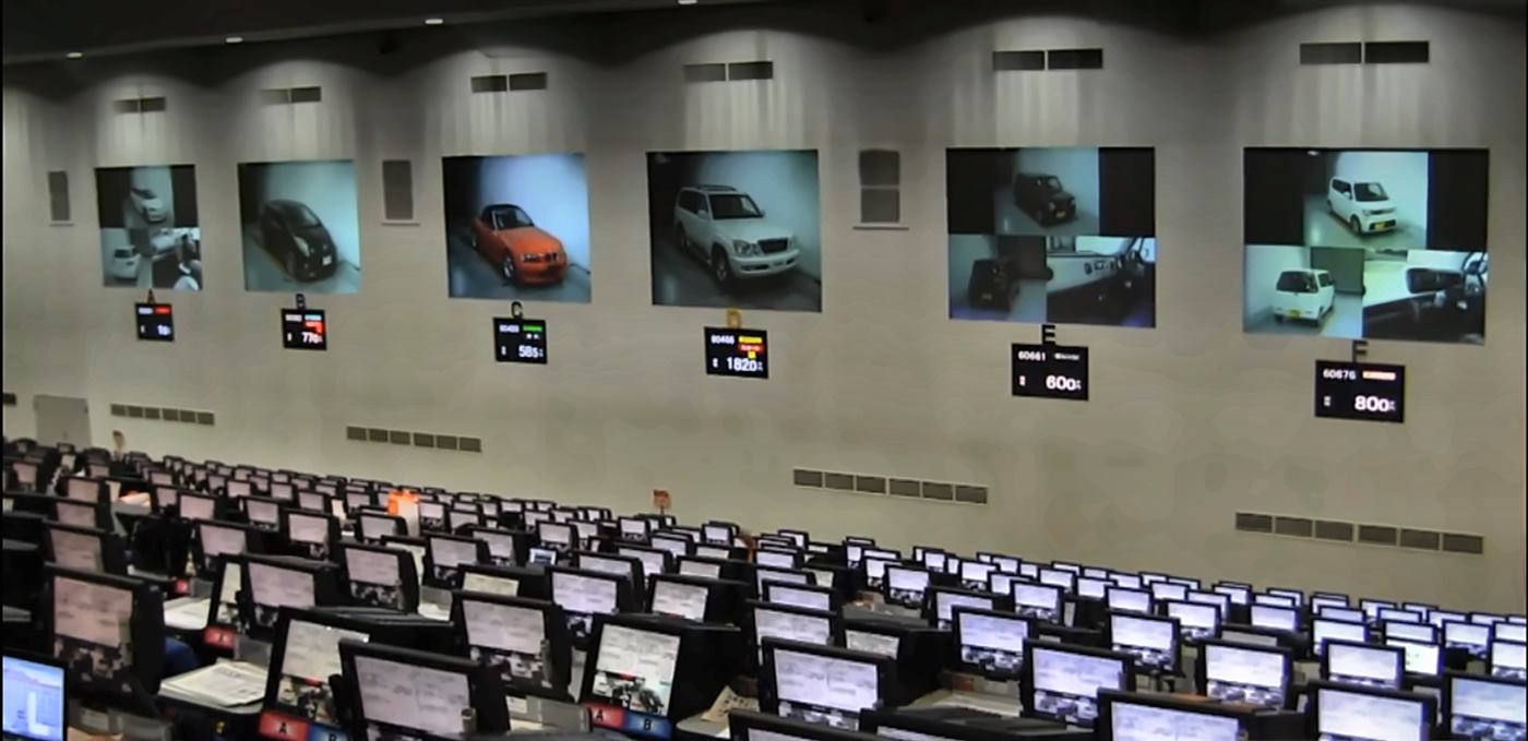 Japanese car auction hall with six lanes on screen and rows of bidding terminals